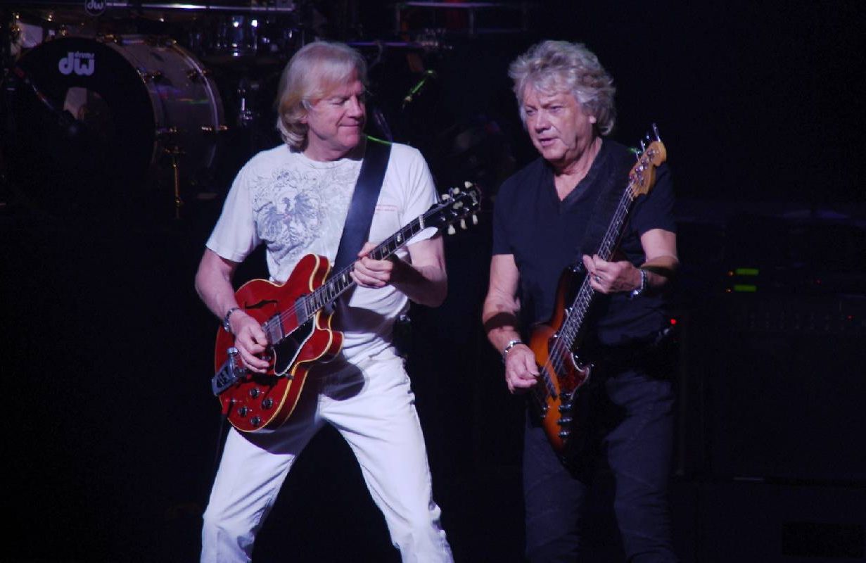 Two men on stage playing a guitar and bass guitar. Next Avenue, Moody Blues,