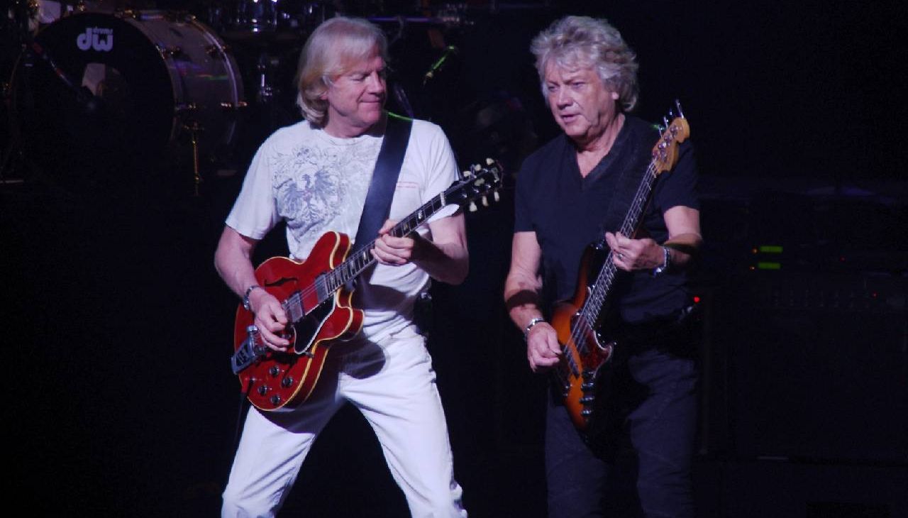 Two men on stage playing a guitar and bass guitar. Next Avenue, Moody Blues,