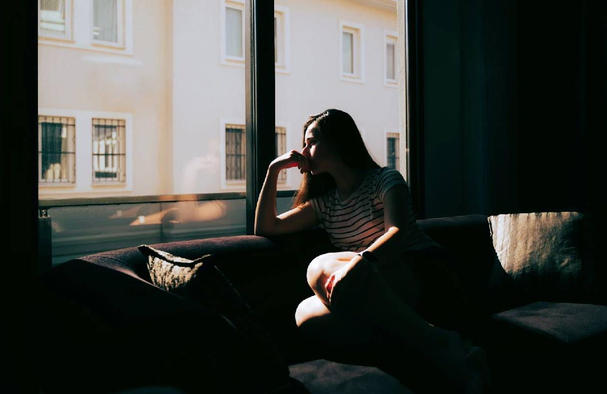 A woman looking out of a window in a darkened apartment. Next Avenue, survivor's checklist, widow, widower