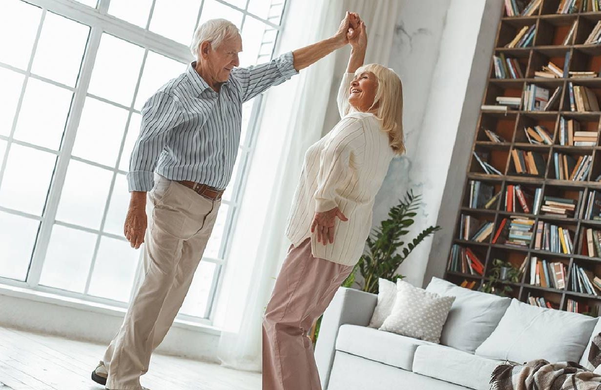 Two older adults dancing together at home. Next Avenue