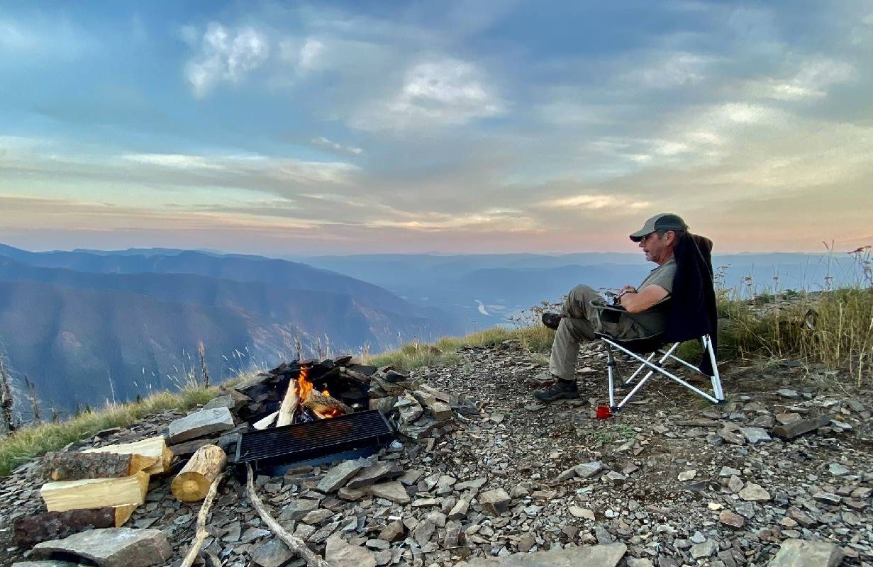 A man sitting on top of a mountain campsite. Next Avenue, camping, road trip
