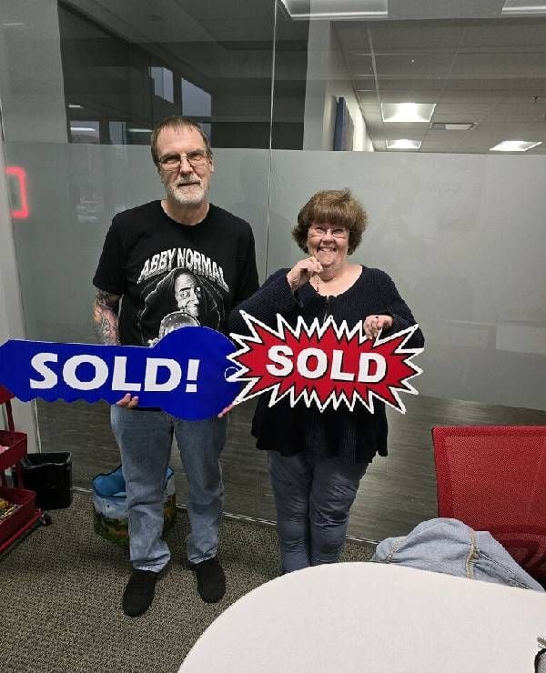 Image of the author and her partner holding the "sold" signs was taken in their real-estate broker's office after they closed on the purchase of a new home near Kansas City. Next Avenue, downsizing