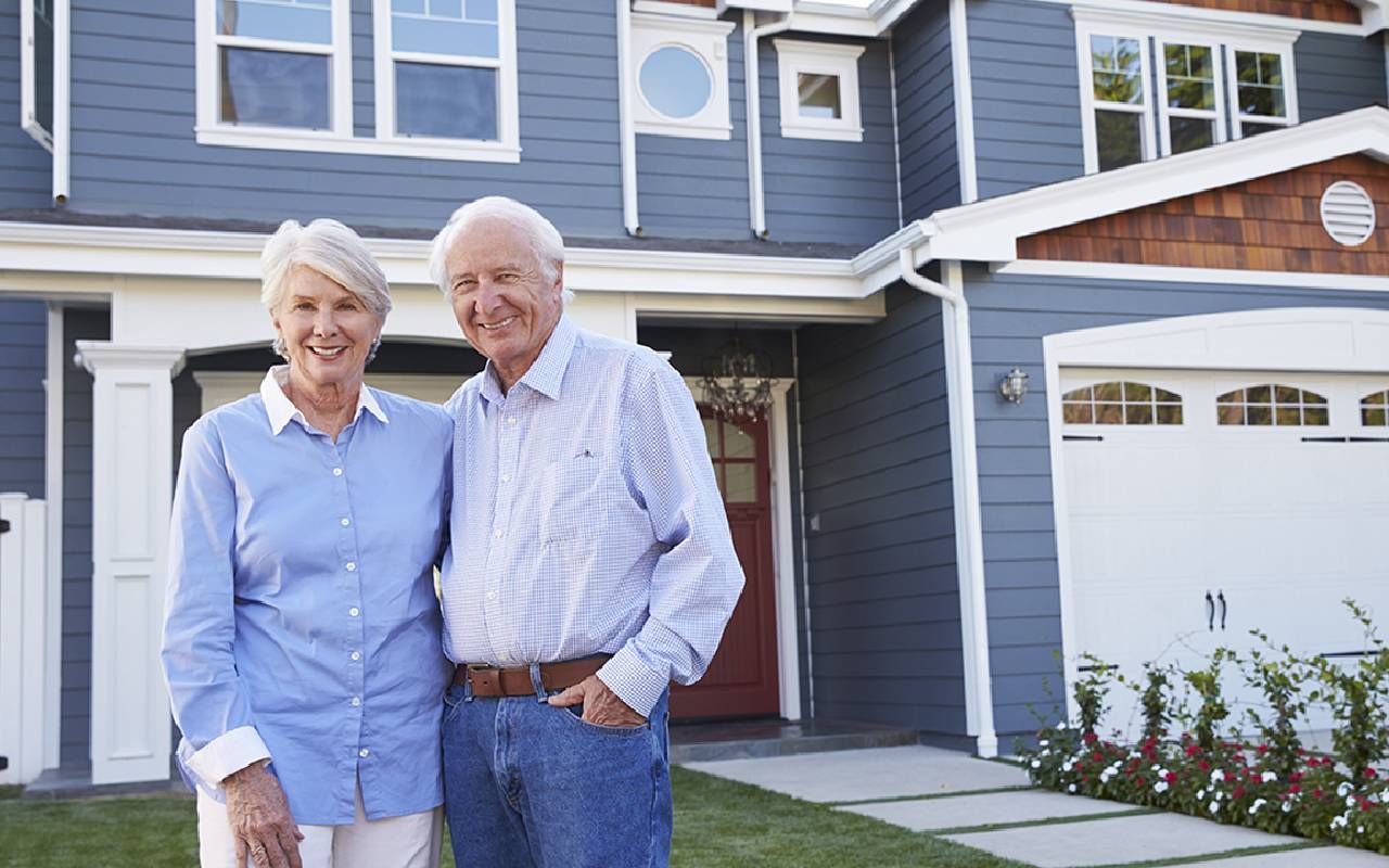 A couple standing outside of their home. Next Avenue