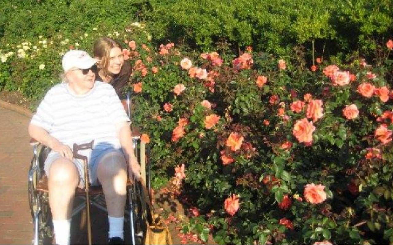 A young person pushing an older person in a wheel chair outside. Next Avenue, grief road trip