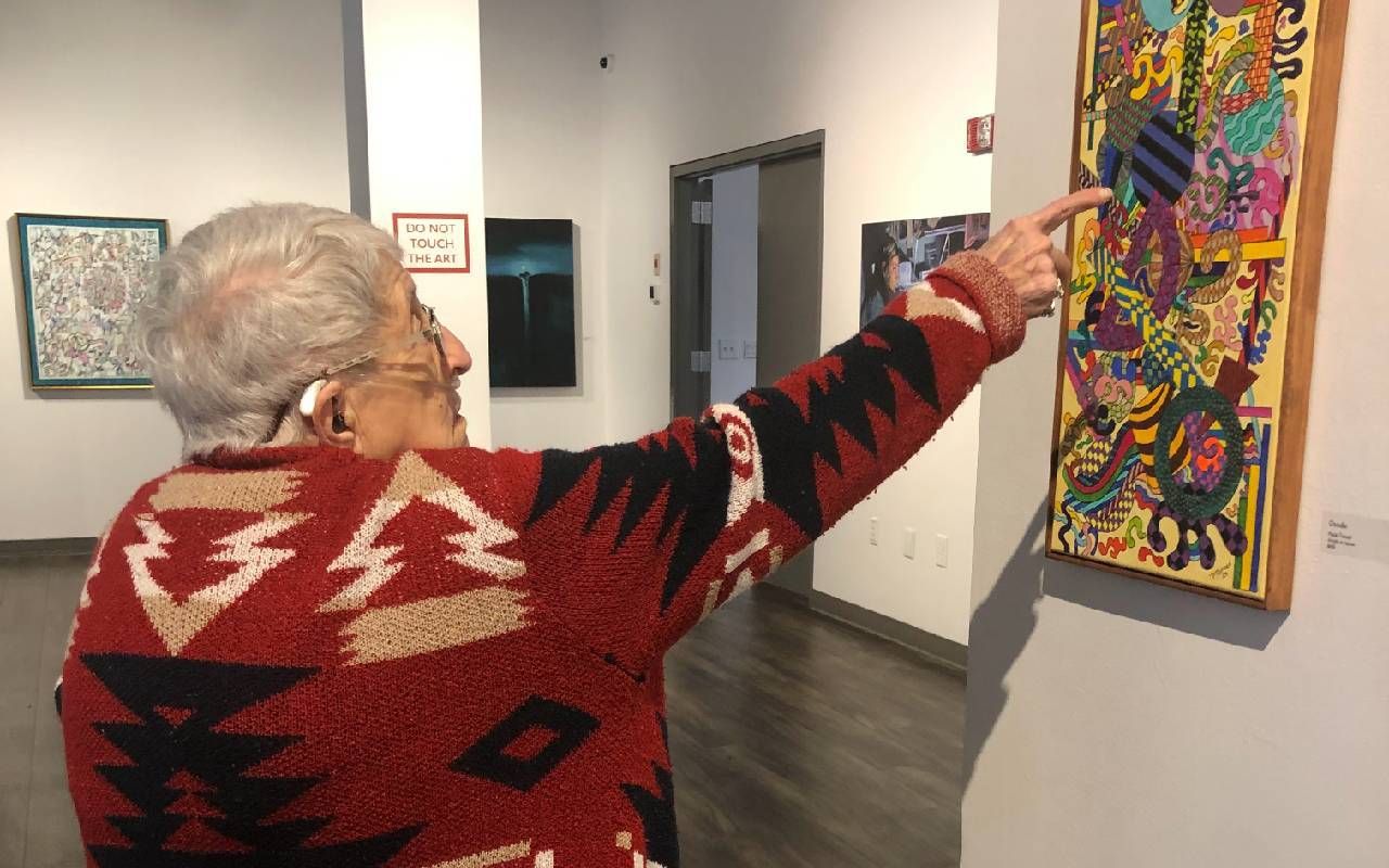 A person pointing at artwork hanging on a gallery wall. Next Avenue, language and art