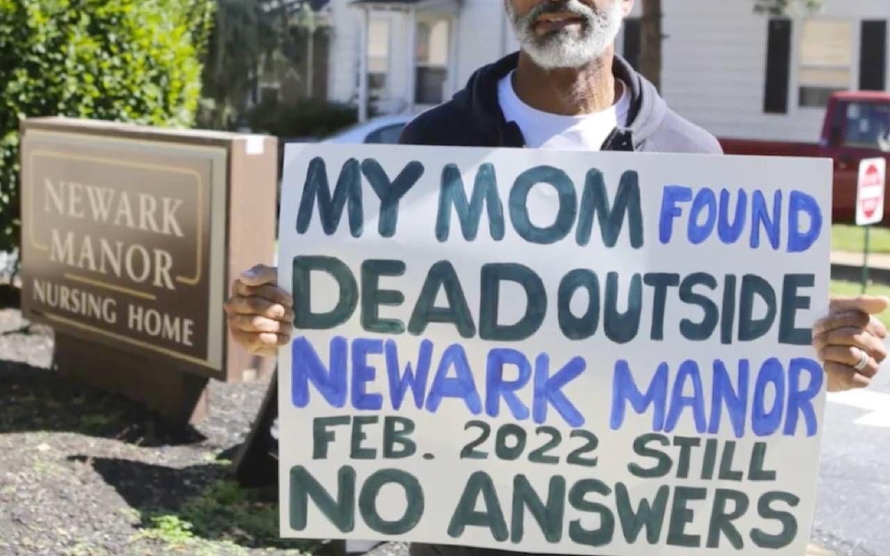 A person holding a sign that says "My Mom found dead outside Newark Manor Feb. 2022 Still no answers." Next Avenue, neglect, nursing homes, No Country for Old People