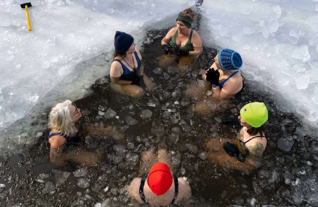 A group of people sitting in icy water. Next Avenue, cold plunge