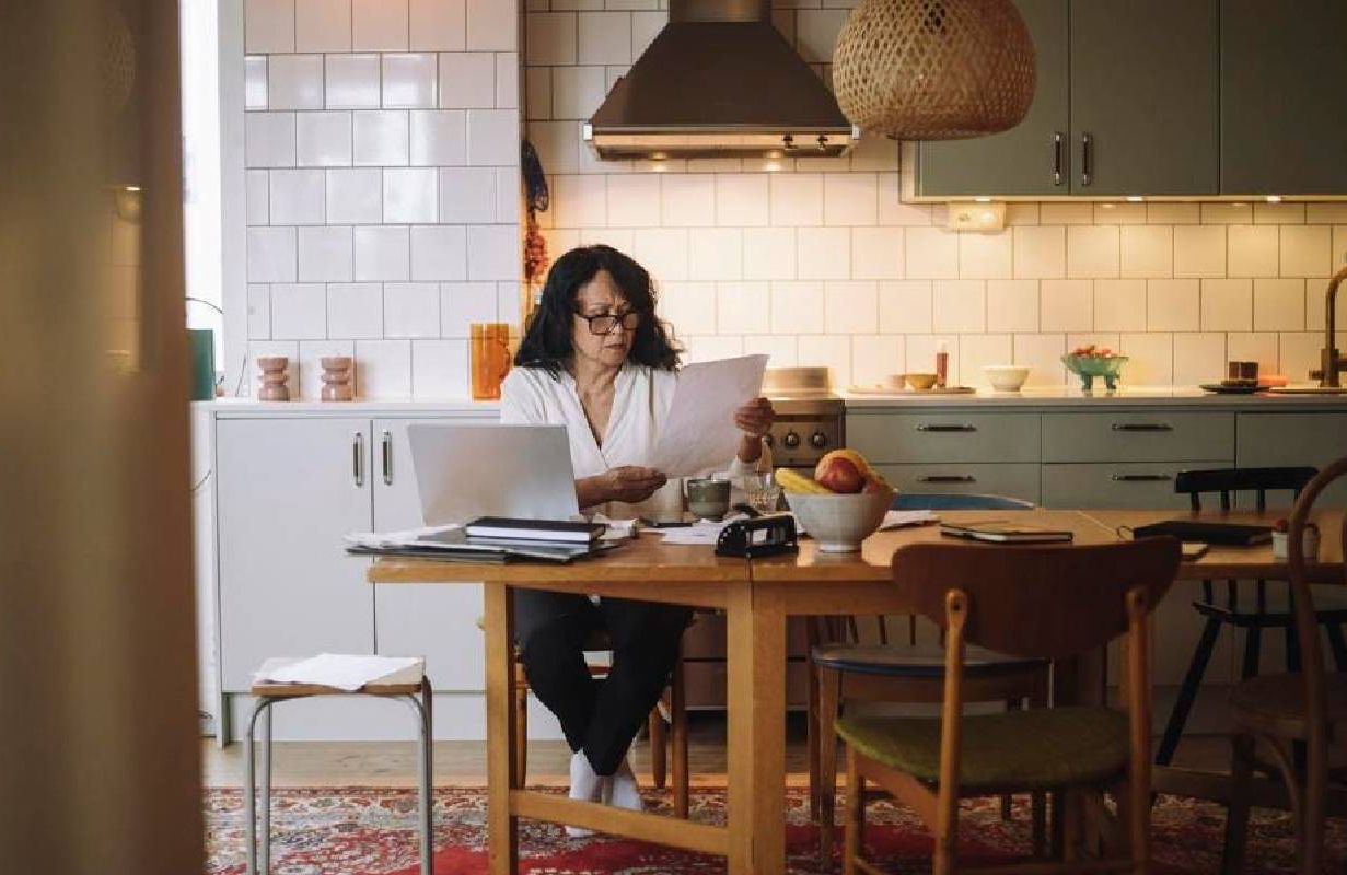 Single woman examining financial bill while sitting with laptop on dining table at home. Next Avenue