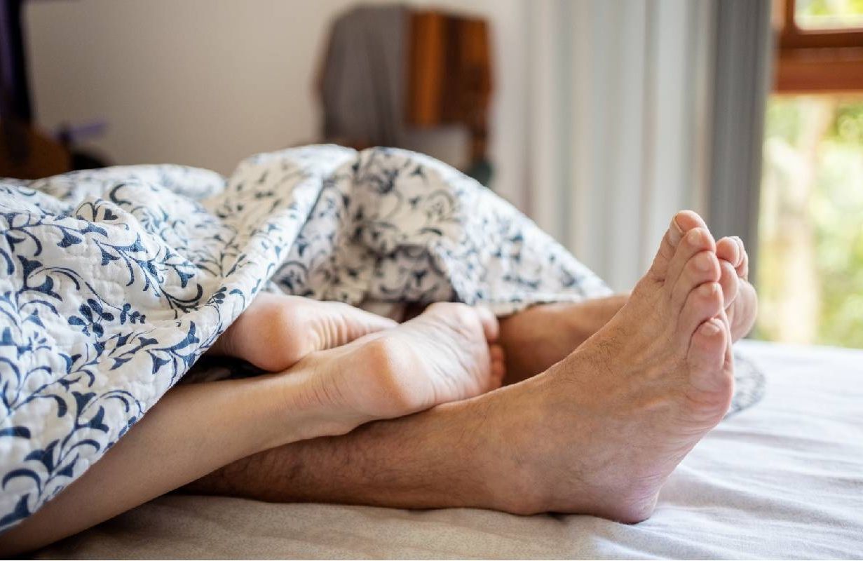 Feet of a romantic couple under the sheets on the bed. Next Avenue