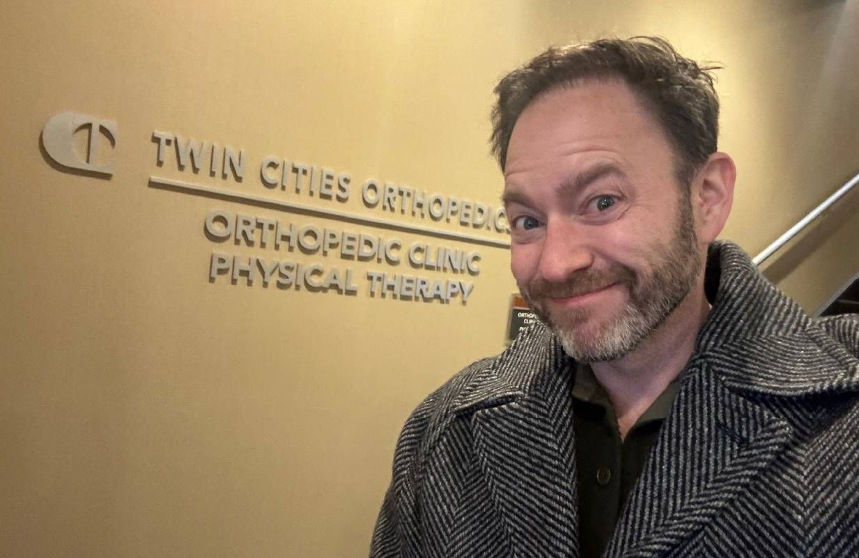A man smiling in front of a sign for a health clinic. Next Avenue