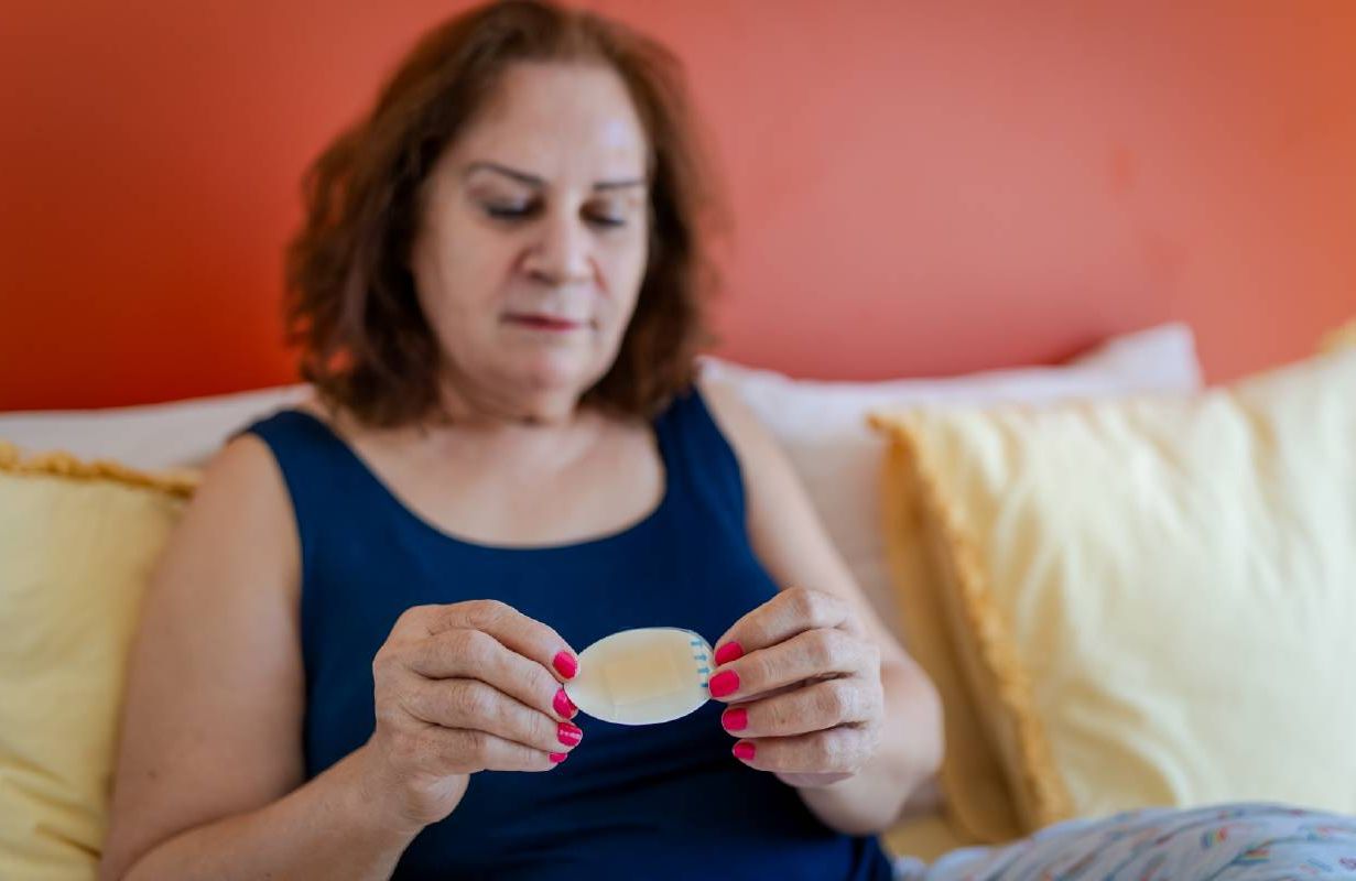 A woman holding up a transdermal estrogen patch for hormone replacement therapy. Next Avenue, menopause