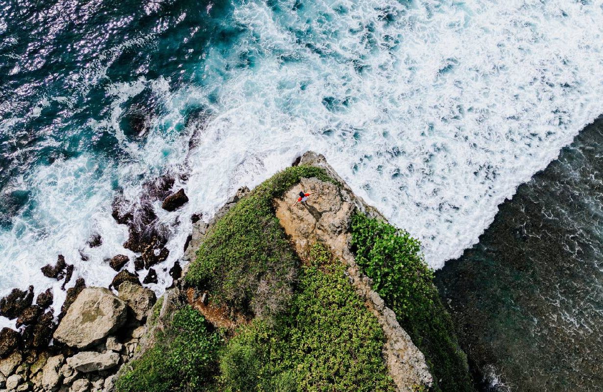 A birds-eye view of a person on a cliff overlooking the ocean