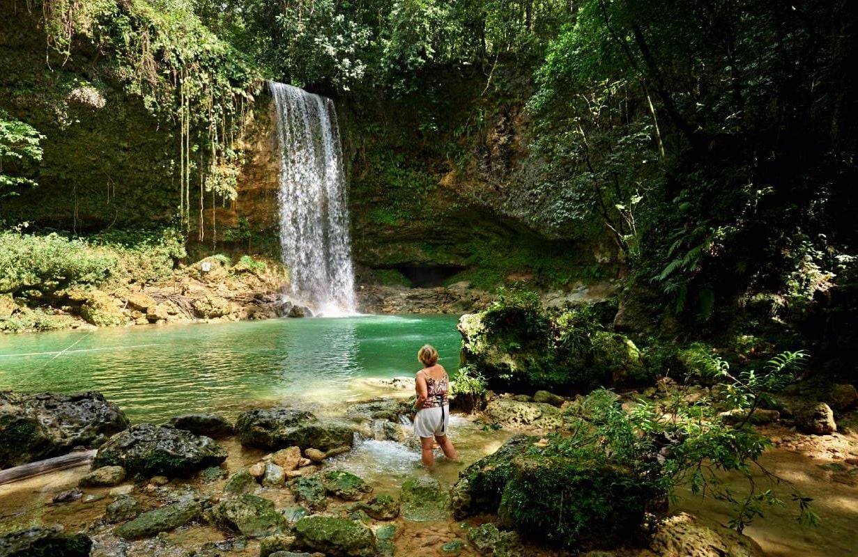 An older woman woman standing and enjoying view of natural pool and 20 meter high waterfall. Next Avenue, slow travel