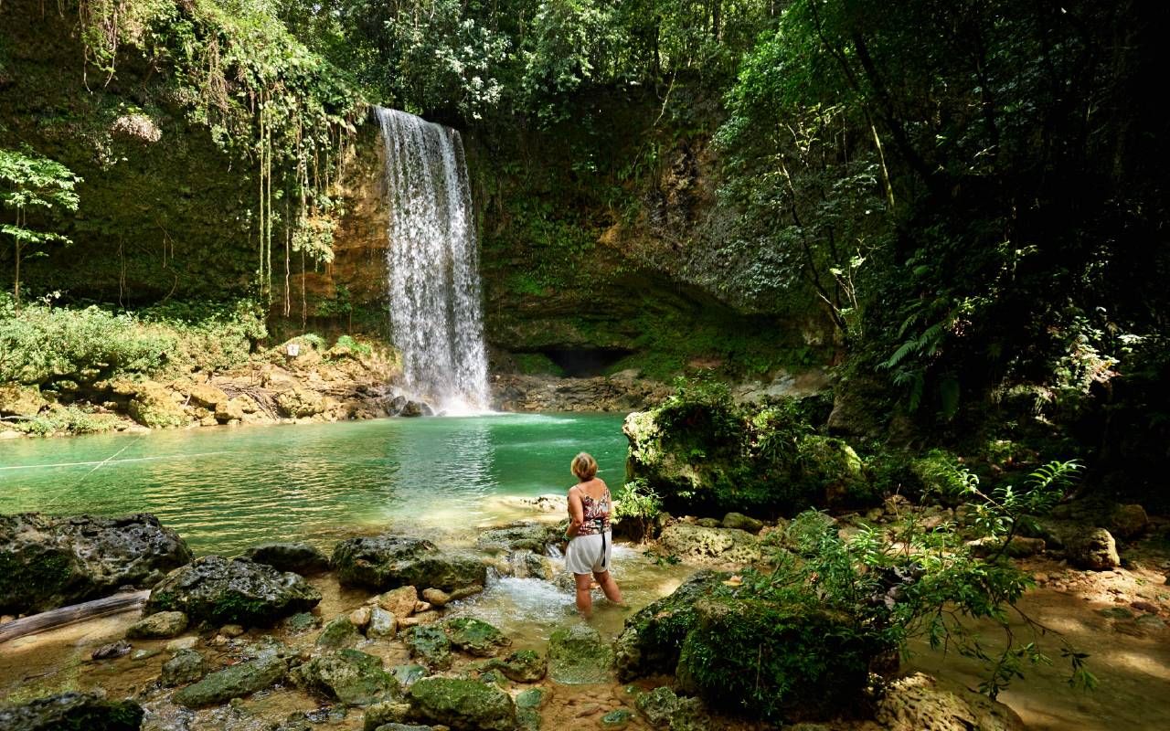 An older woman woman standing and enjoying view of natural pool and 20 meter high waterfall. Next Avenue, slow travel