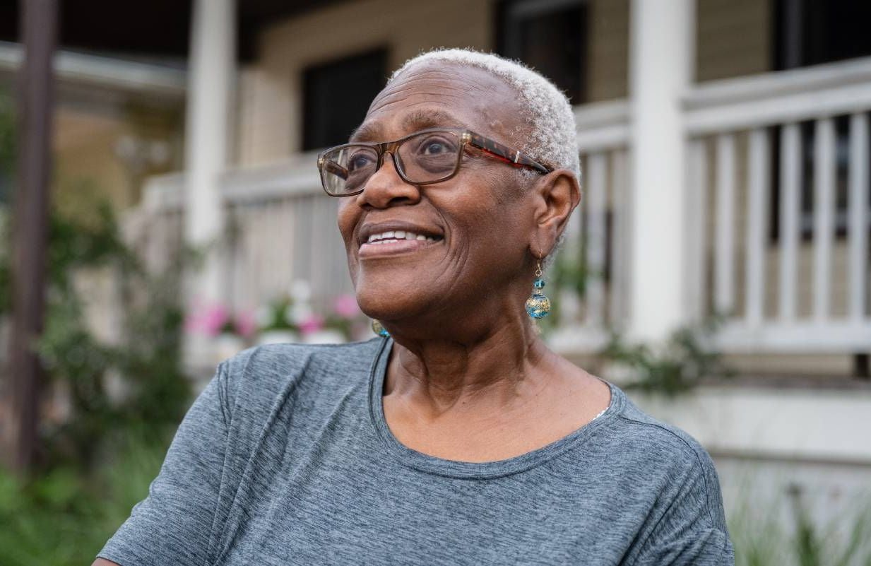 A wretired woman standing in front of her house. Next Avenue, retirement, debt