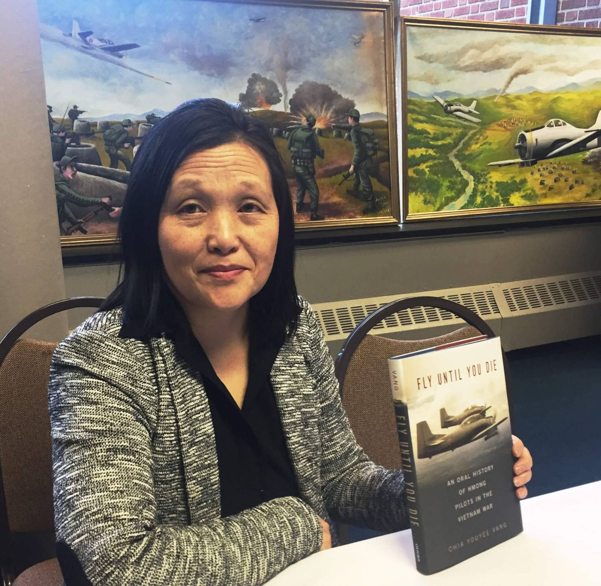 Hmong author holding a book titled "Fly Until You Die"