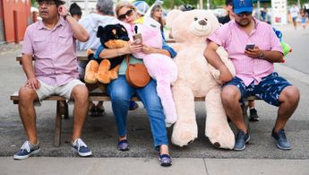 a group of people sit on a bench with a person in a bear garpeoplet