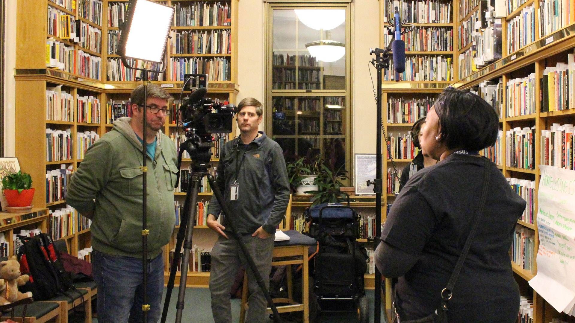 A man conducts a video inyterview with a woman inside of a library