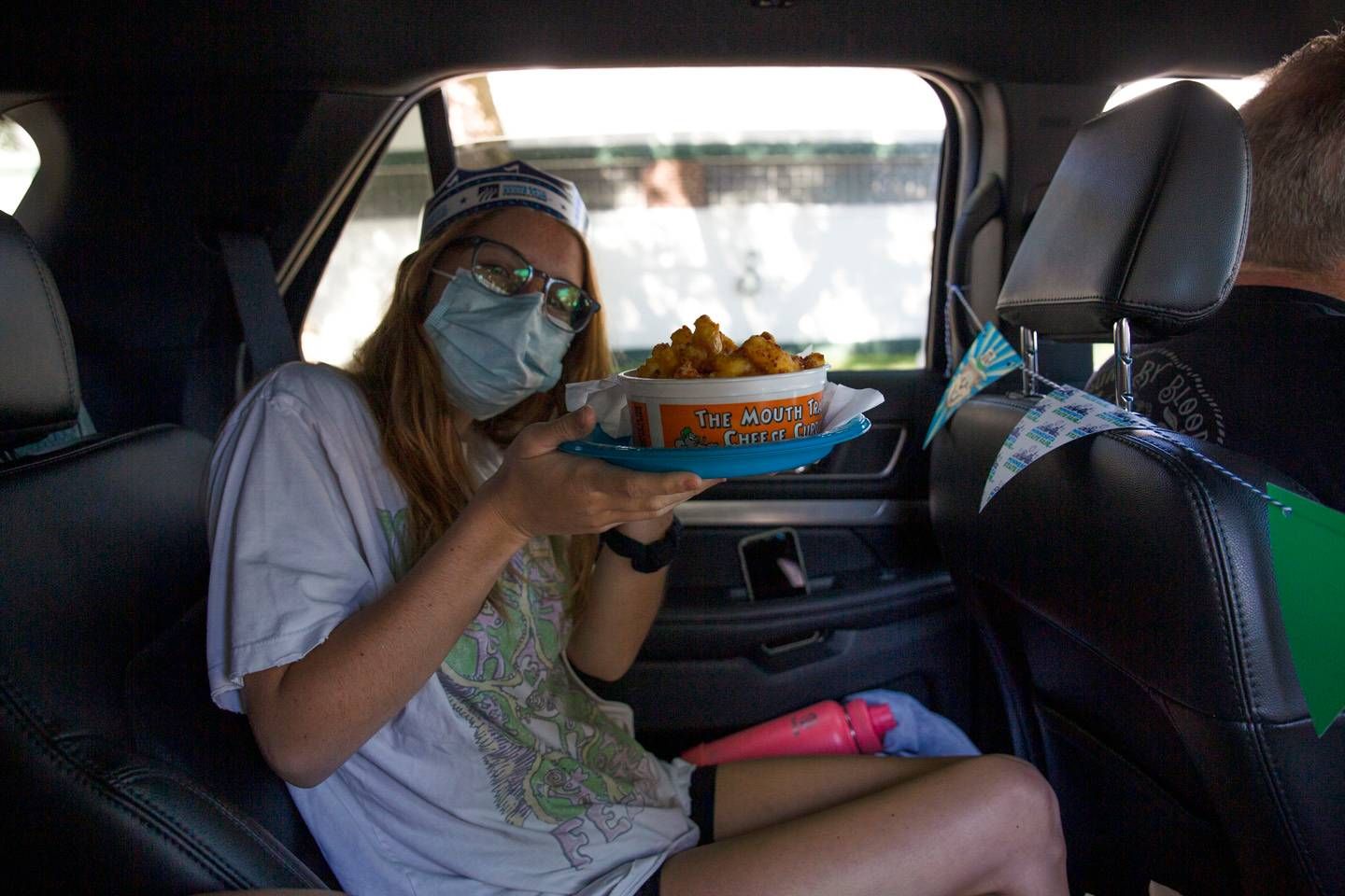 A white girl with a mask and a crown holds a bucket of cheese curds