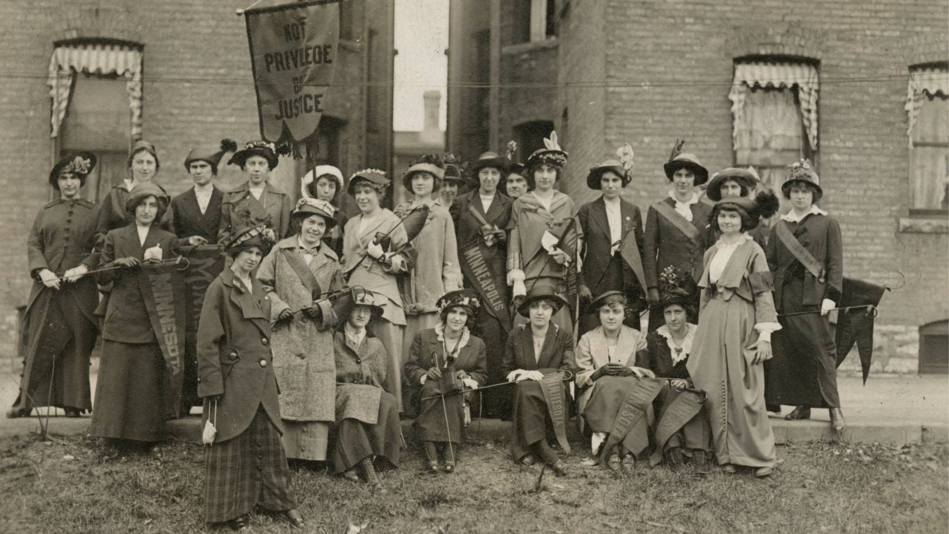 Black and white photo of women gathered in a group holding pennants