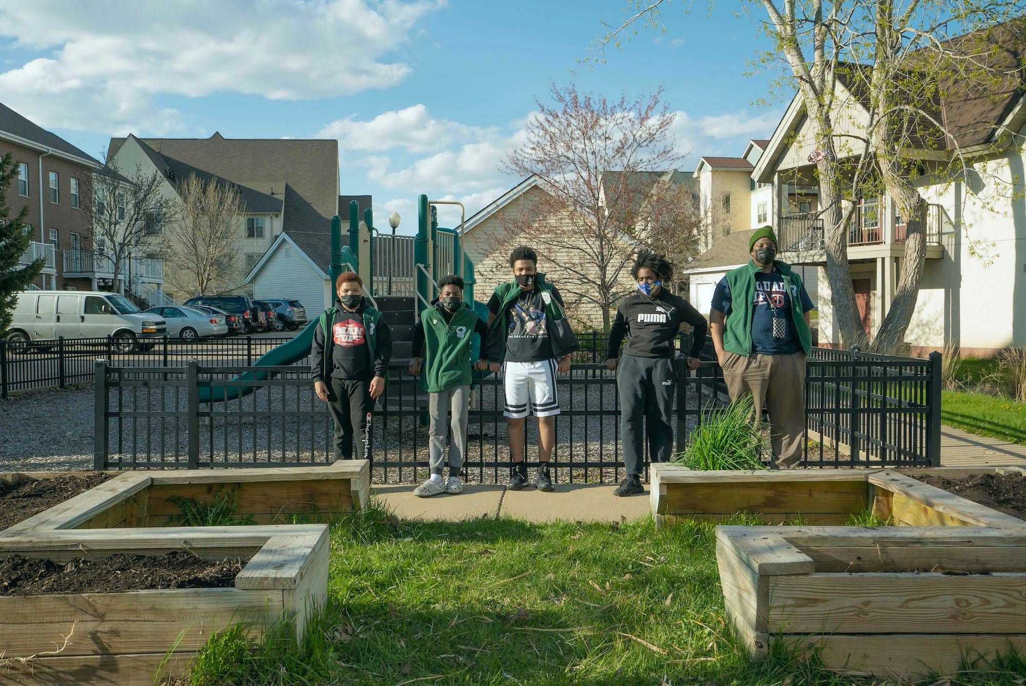 A group of youth stand against a metal fence.