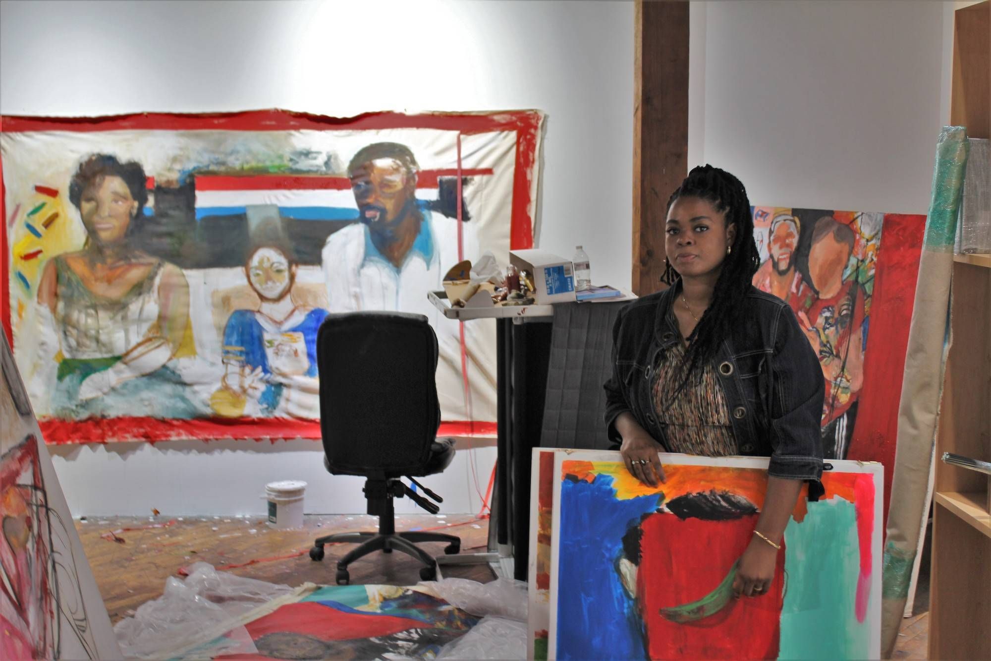 an artist stands with her artwork in a studio.