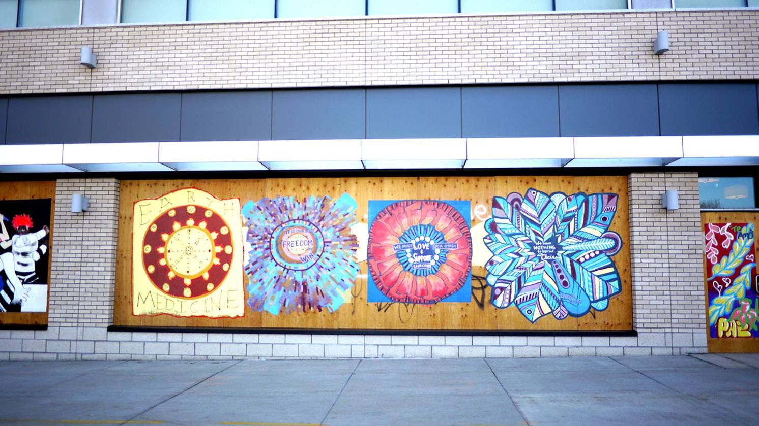 Colorful murals painted on the plywood that covers storefront windows.