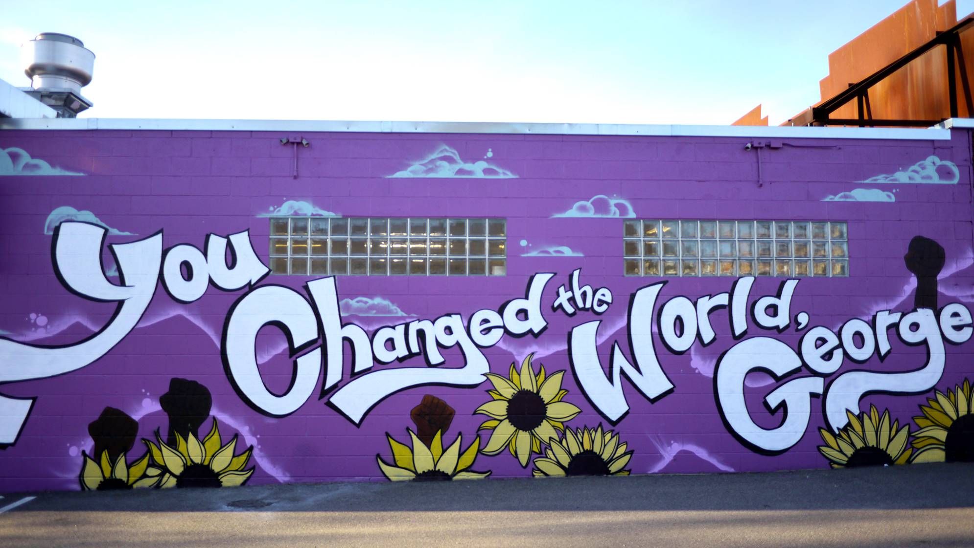 A building wall painted purple with "You Changed the World George" painted in white.