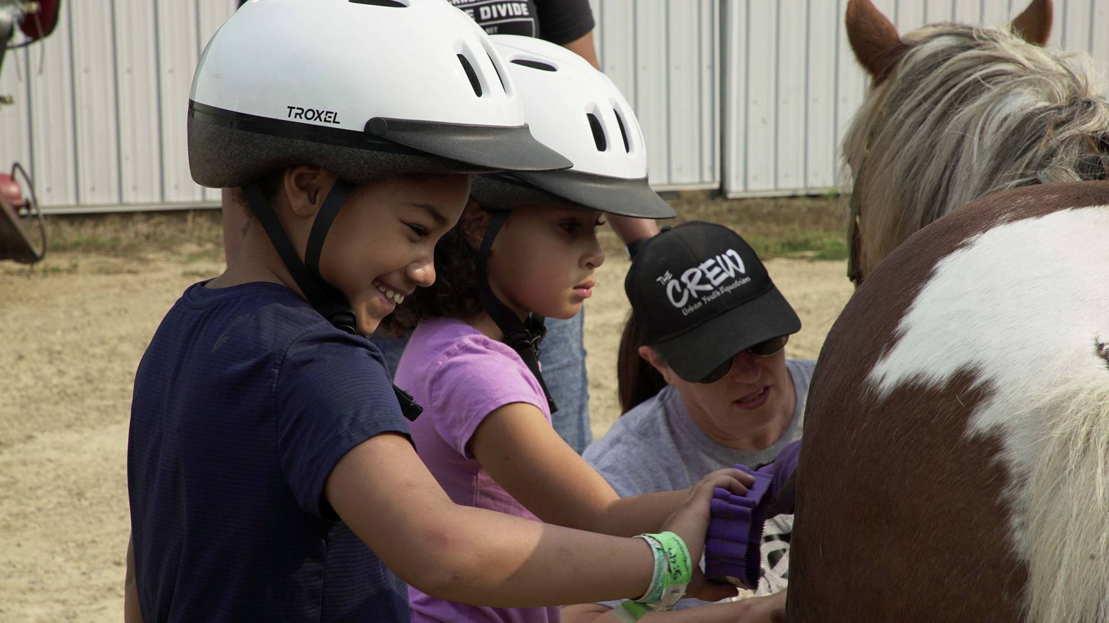 Two young girls brush a pinto pony.