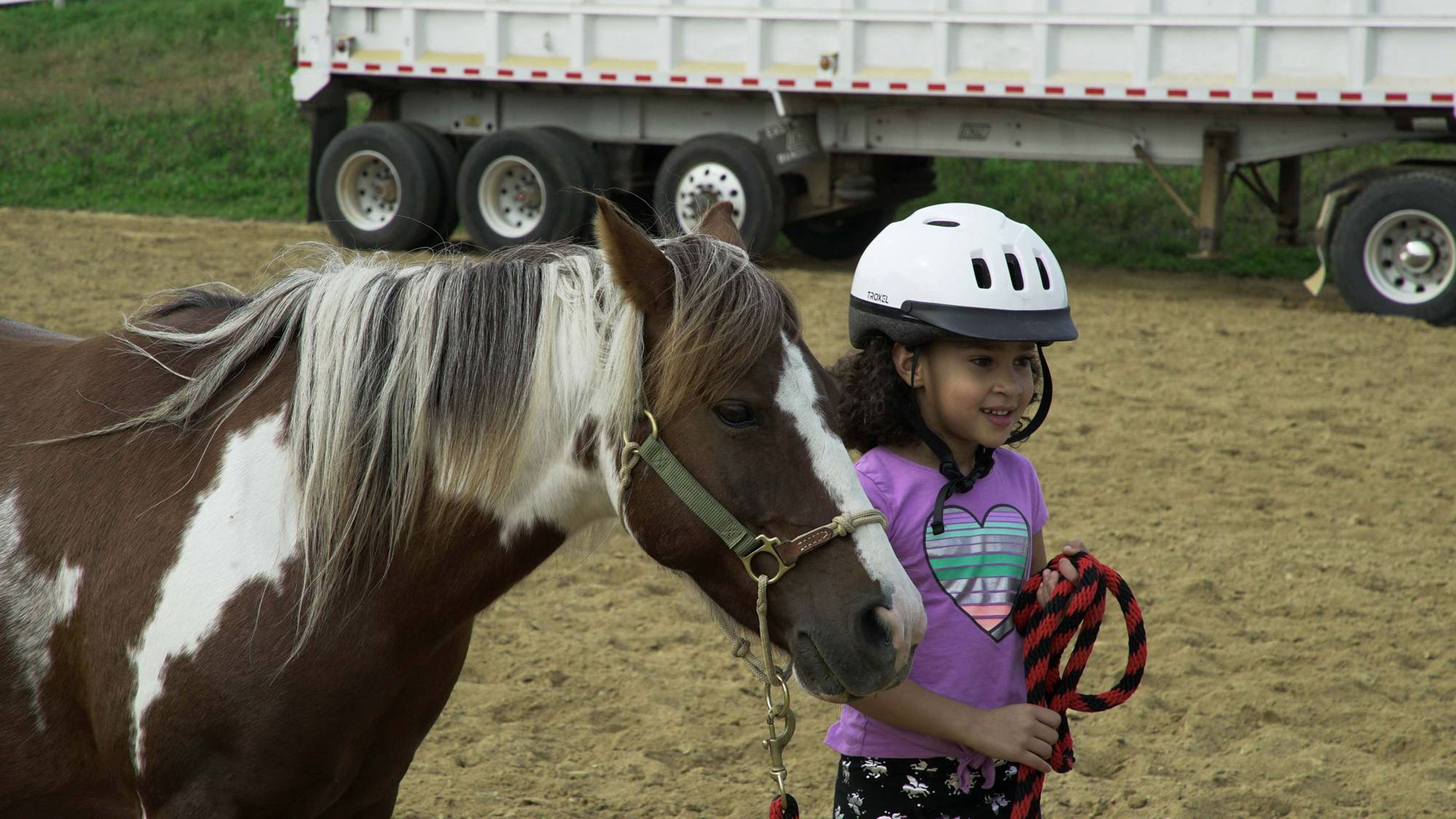 A young girl smiles while leading a small pony.