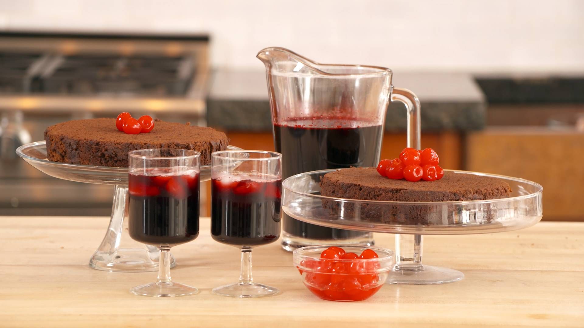 Two Jamaican Fruitcakes garnished with cherries and two glasses and a pitcher of sorrel wine