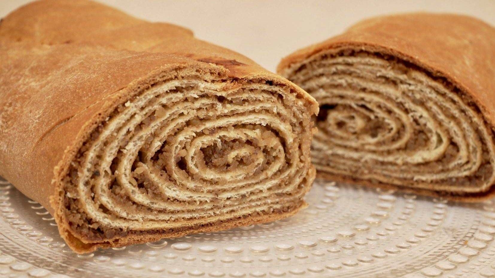 A loaf of potica cut in half on a glass platter revealing the swirled layers of walnut filling.