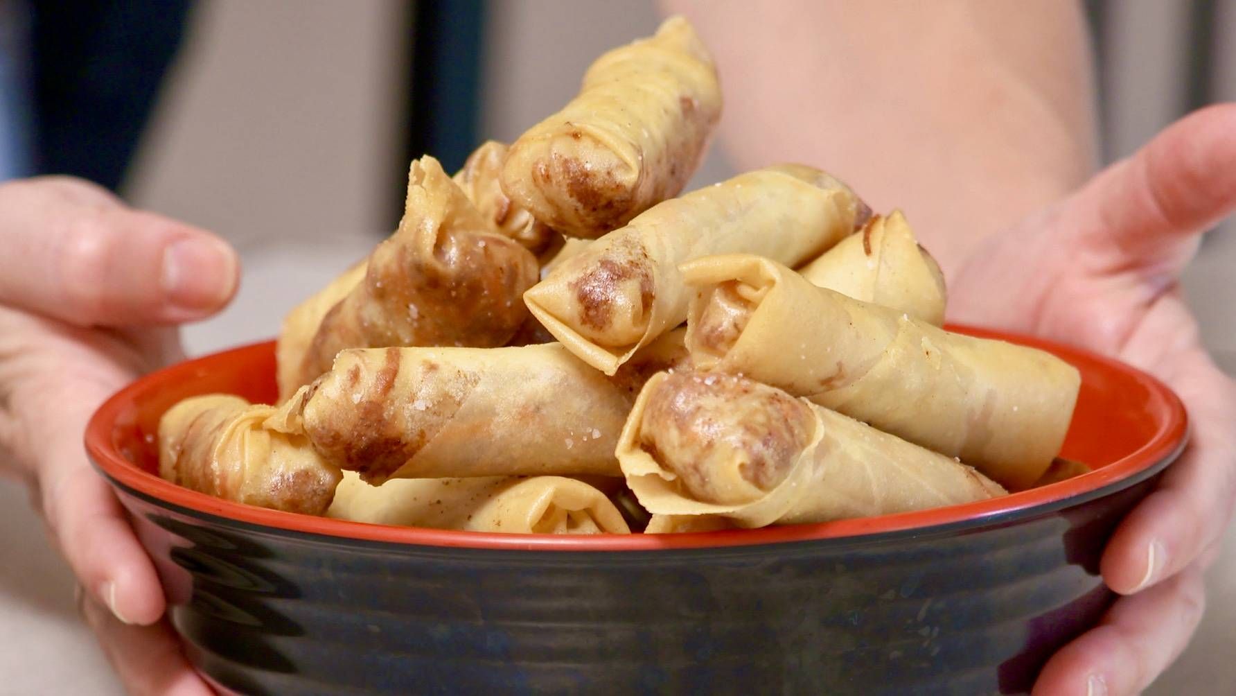 Hands placing a bowl of egg rolls on a table.