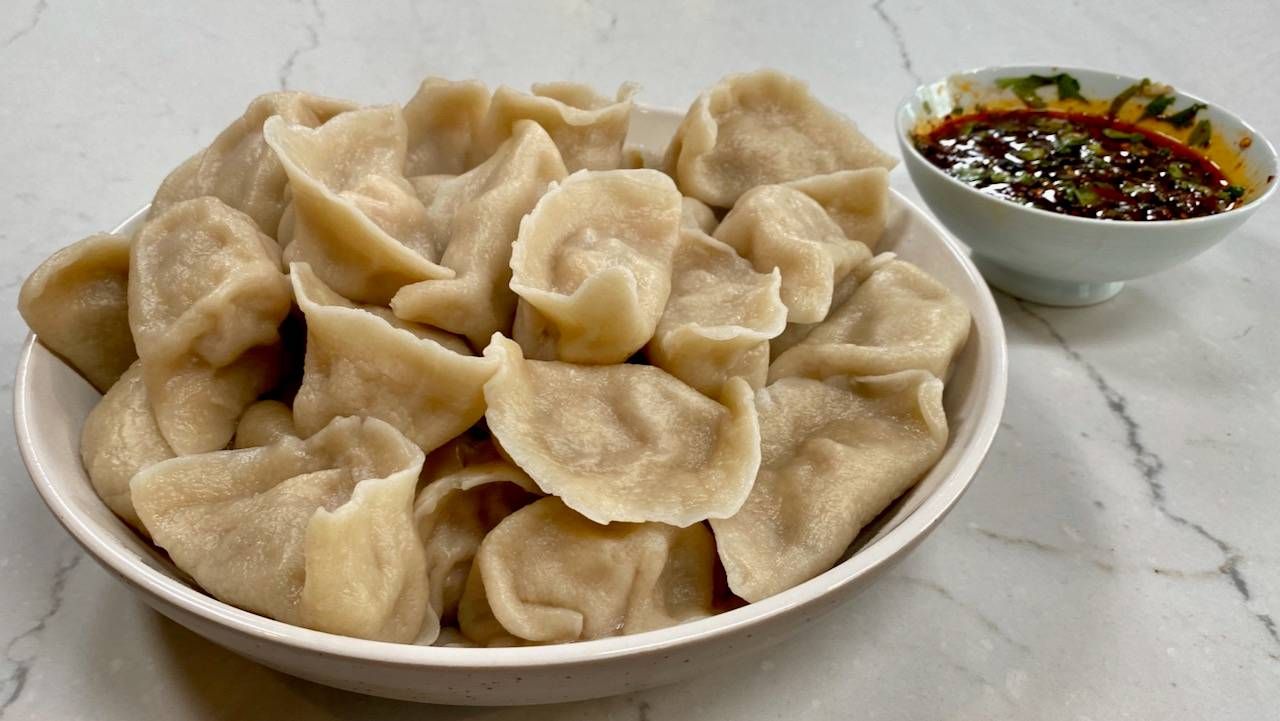 Plate filled with dozens of dumplings with a small bowl of sauce next to it