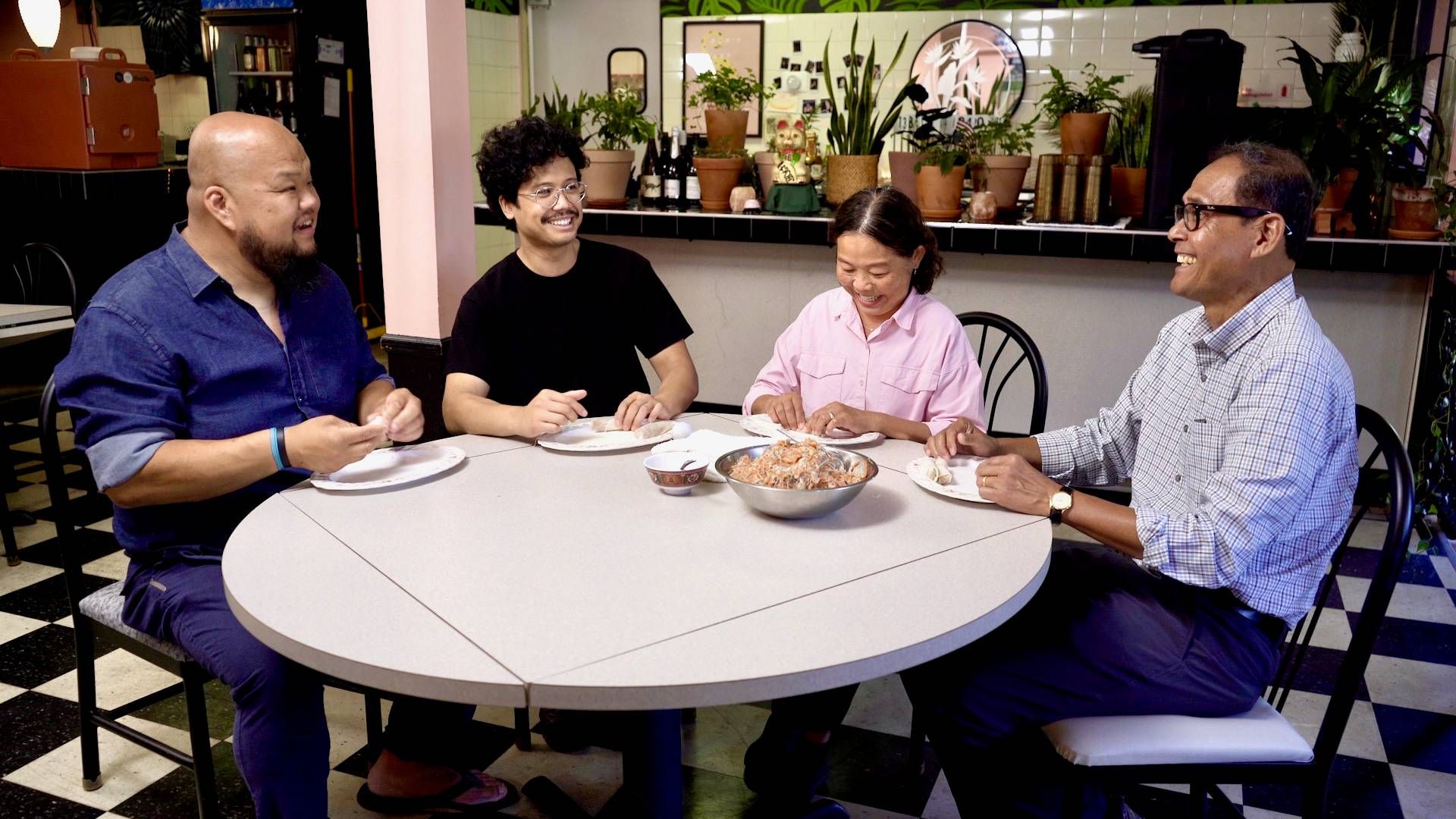 Chef Yia Vang at table wrapping egg rolls with chef Bunbob Chhun and his parents.