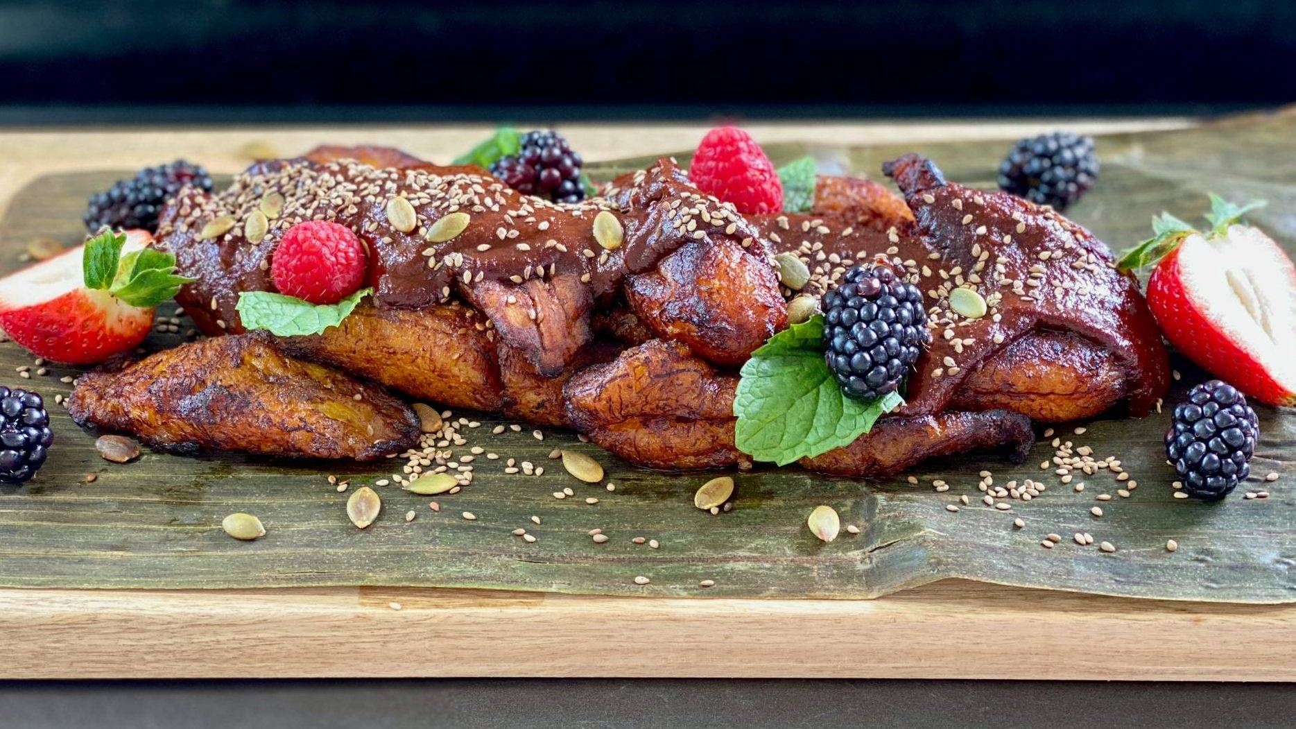 Photo of fried plantains covered in Guatemalan mole sauce, garnished with fresh berries.