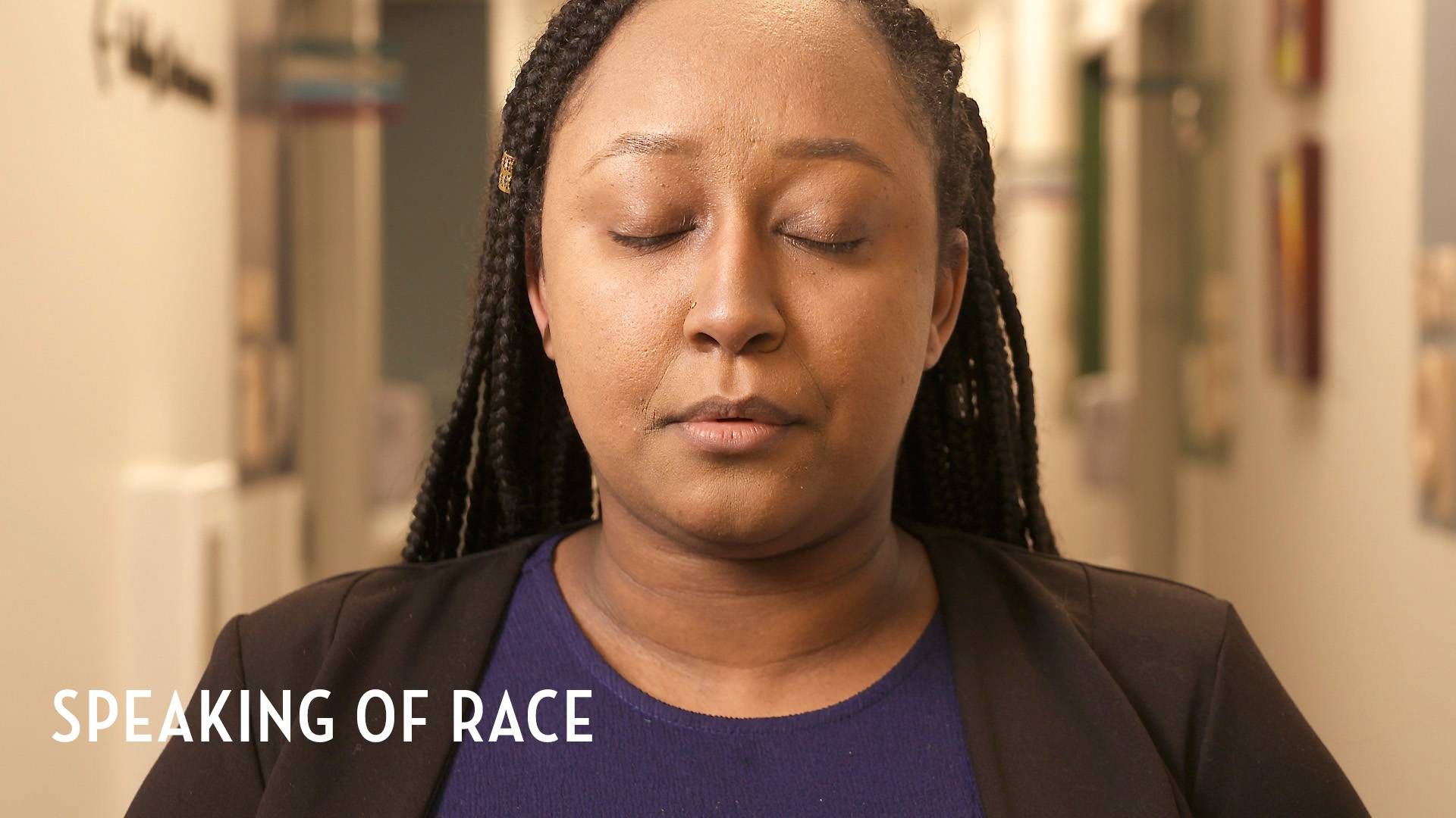 Black female doctor in a clinic hallway facing camera, closing eyes and exhaling