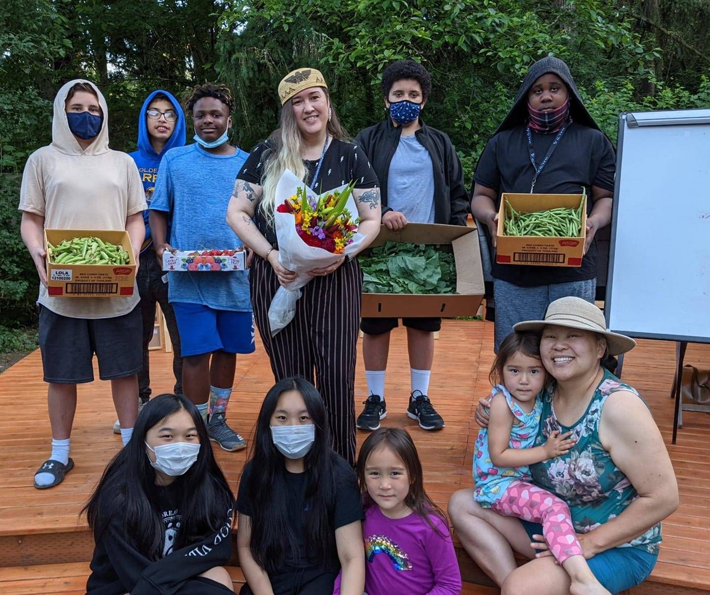 A photo of young adults and adults, holding fresh vegetables and flowers.