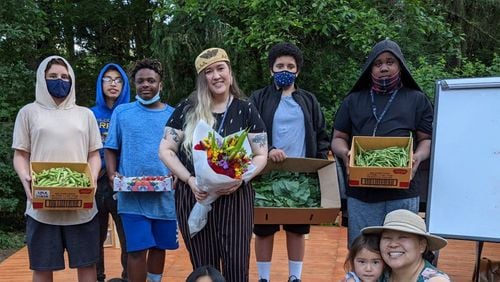A photo of young adults and adults, holding fresh vegetables and flowers.