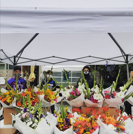 Three people stand behind a row of beautiful floral bouquets.