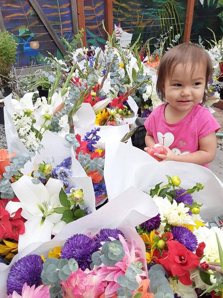 A smiling toddler stands amidst multiple bouquets of flowers.