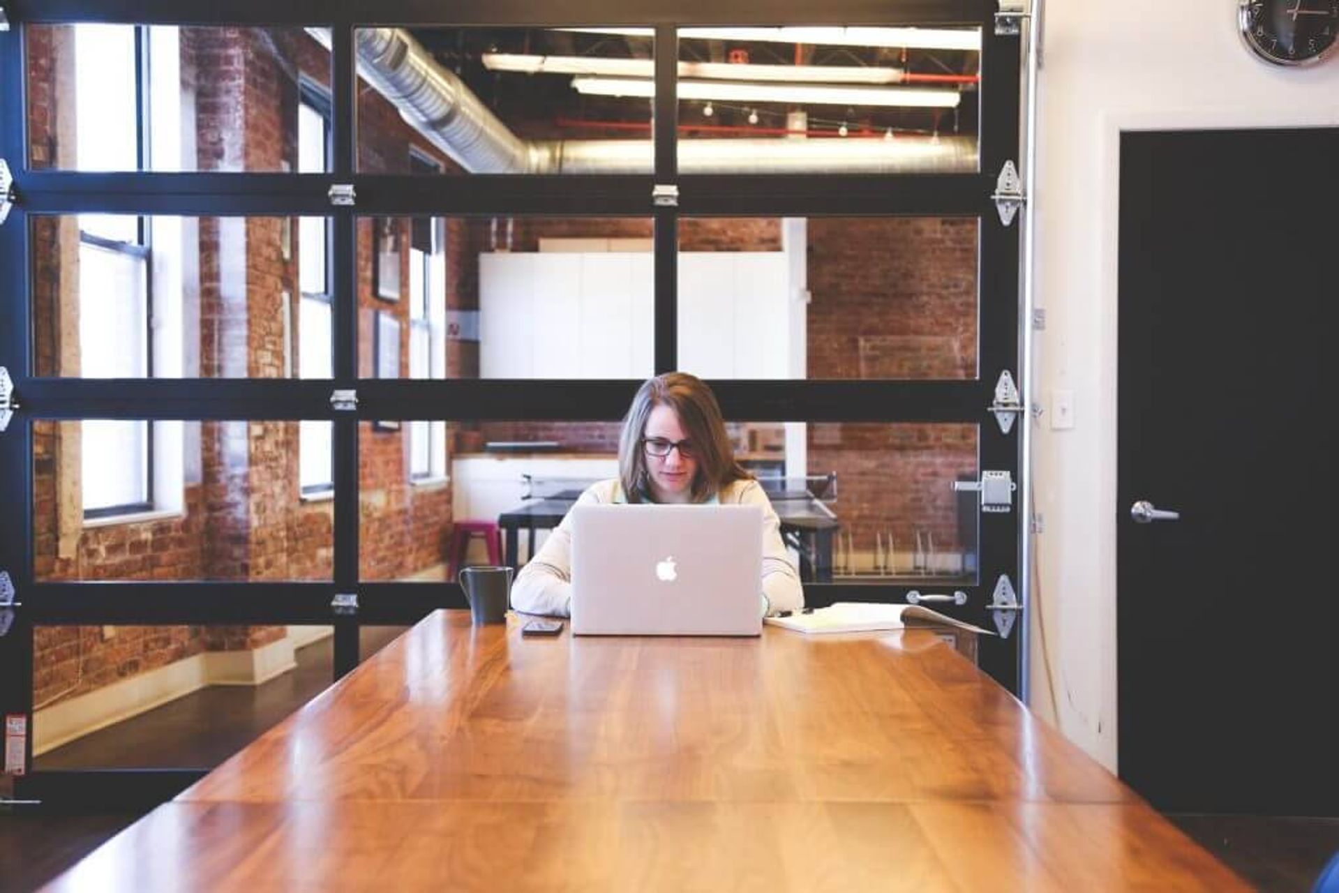 Woman sitting at the end of an empty conference table working on a laptop.