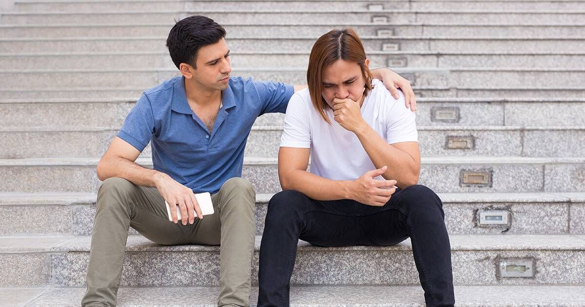 Portrait of serious handsome young man supporting his depressed friend and holding hand on his shoulder. They are sitting on outdoor stairway. Friend support concept. Front view. Rewire PBS Love Parents' Divorce