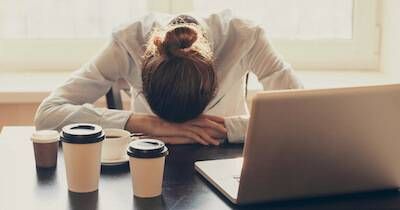 Woman with her head on her desk in front of several cups of coffee. Crisis pbs rewire
