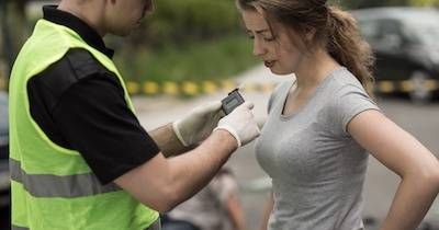 Woman being given a breathalyzer test by a police officer after a car crash. Warrant pbs rewire