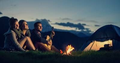 Three friends sit next to a fire and tent as one plays a song on a guitar. Too Much Time With Your Partner pbs rewire