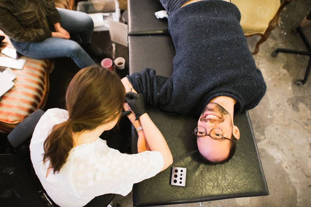 Photo of a man laying on a table to get a tattoo. Rewire PBS Living stick-and-poke