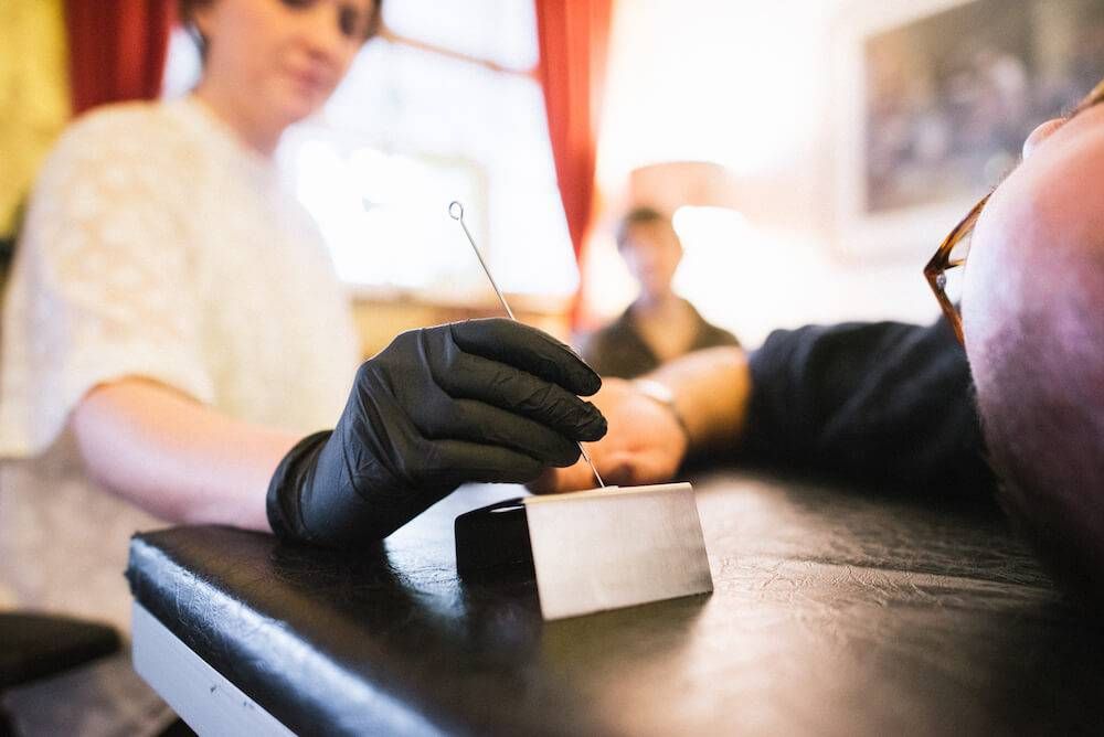 Close up on a gloved hand holding a long needle. Rewire PBS Living stick-and-poke