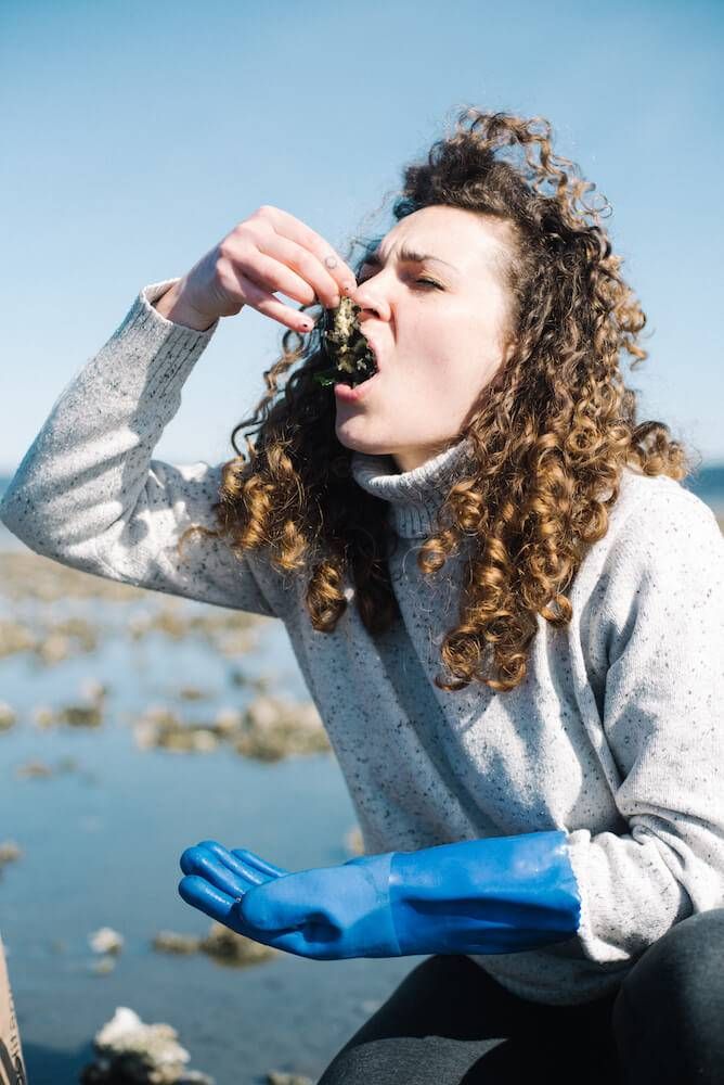 Photo of Kaelyn Handsel eating an oyster fresh from the oyster bed. Rewire PBS Living Oysters