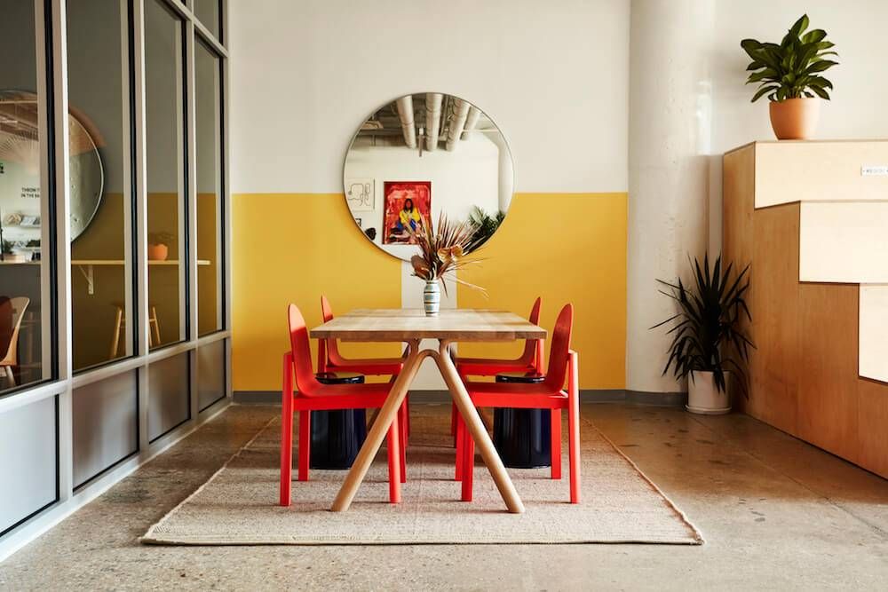 Photo of a breakout space with a wood table and red chairs in a coworking space. Rewire PBS Work People of color
